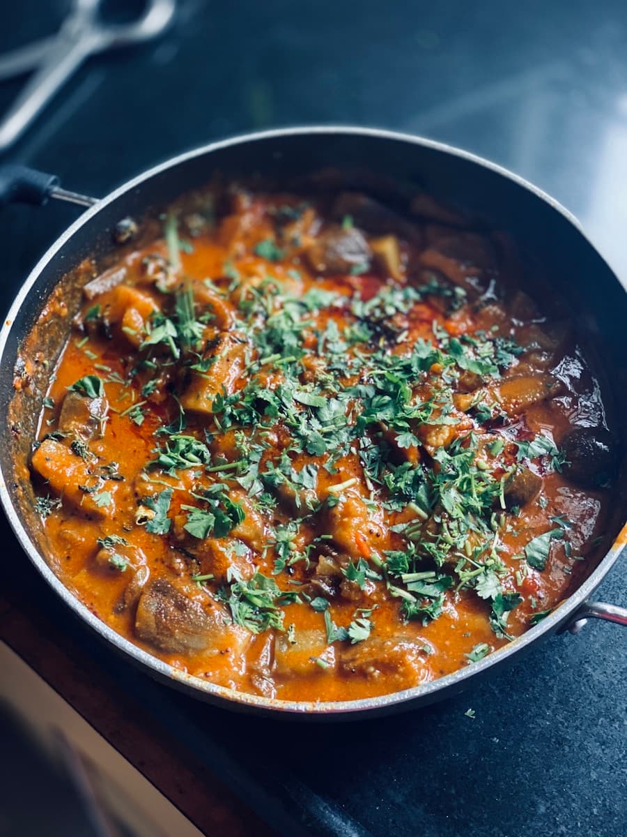 Dum Aloo — golden potatoes in saffron-colored sauce, small copper bowl, dark background