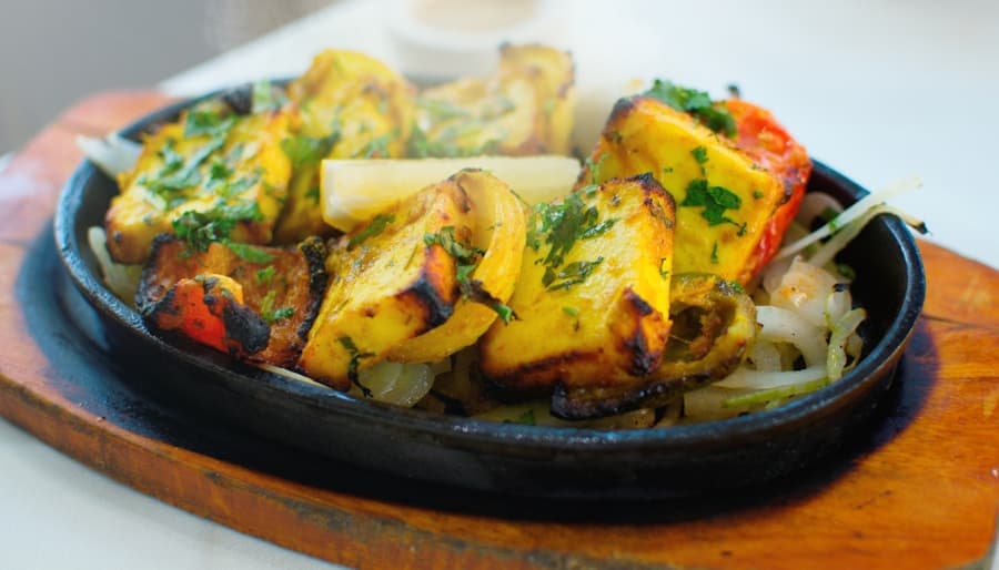 Haak — dark leafy Kashmiri greens in copper pot, rustic surface, warm ambient light