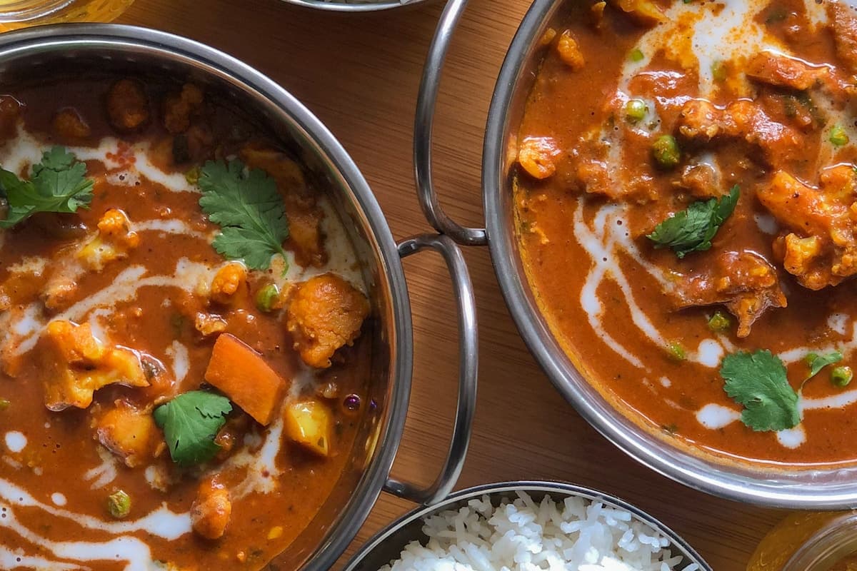 Signature Roghan Josh — deep red braised mutton in copper vessel, candlelight, dark surface